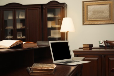 Photo of Old books and laptop on wooden table in library reading room