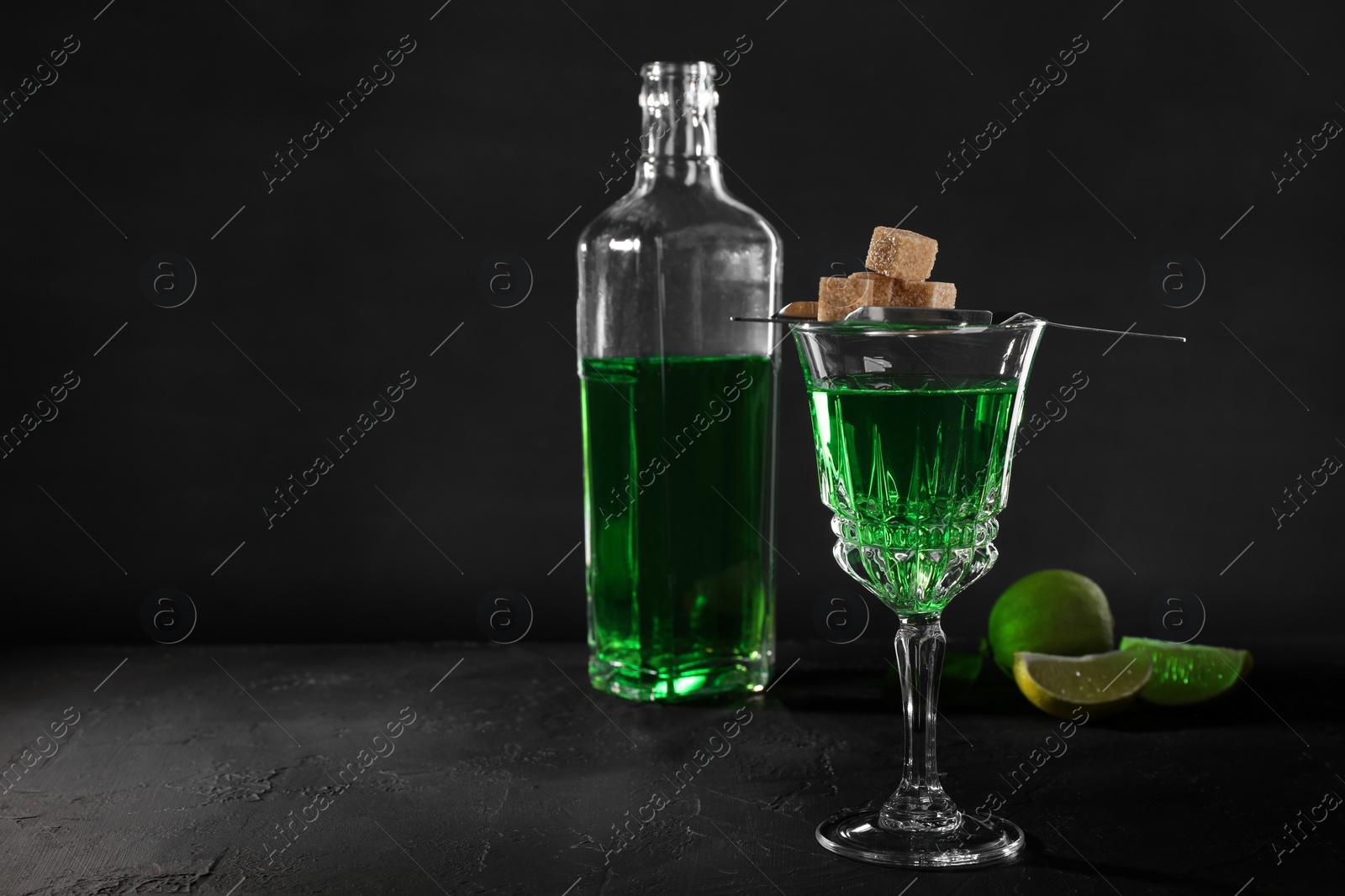 Photo of Absinthe, brown sugar and lime on black table, space for text. Alcoholic drink