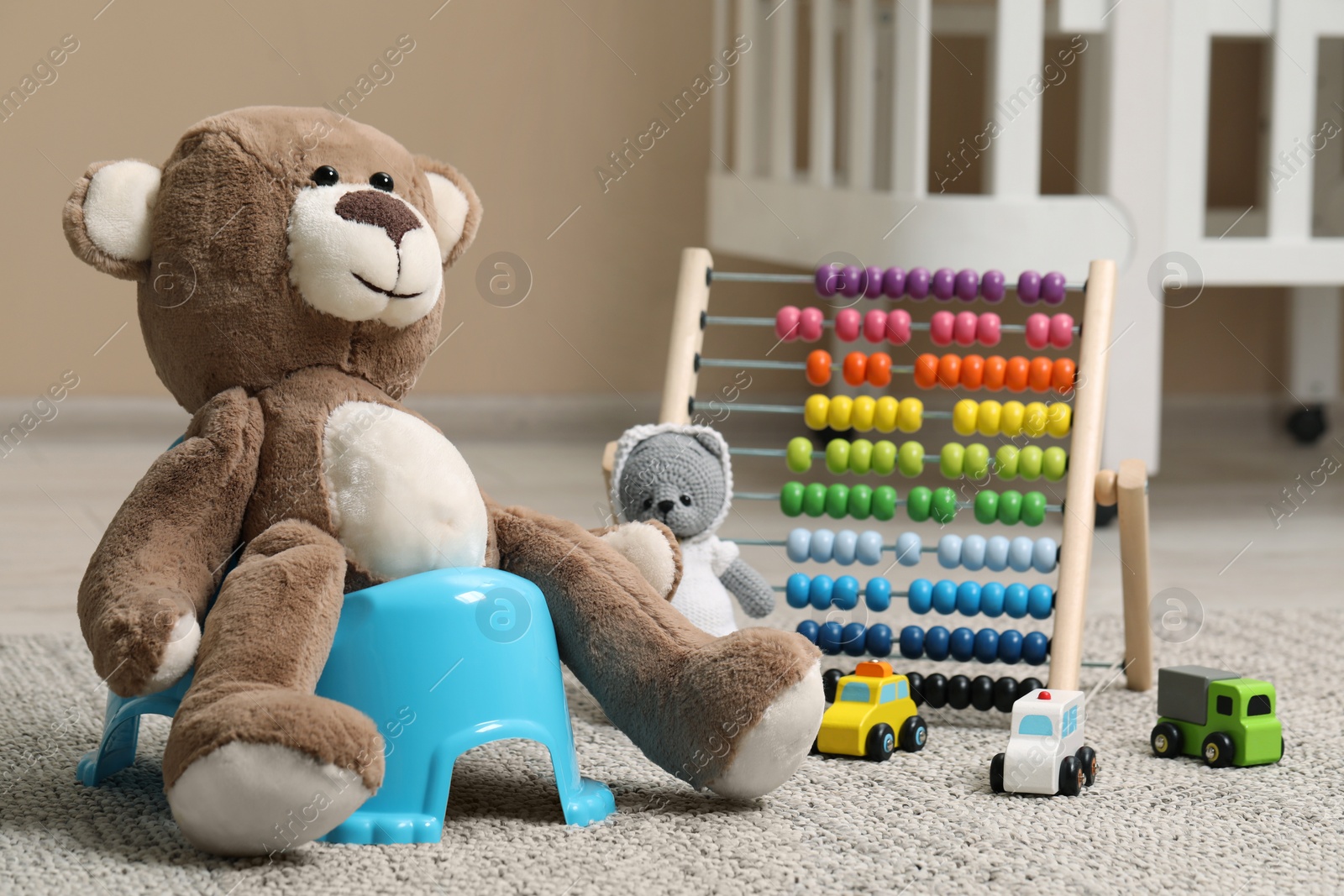 Photo of Teddy bear on light blue baby potty and toys in room. Toilet training