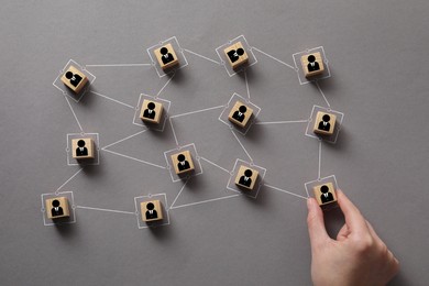 Image of Teamwork. Woman arranging wooden cubes with human icons linked together symbolizing cooperation at grey table, top view