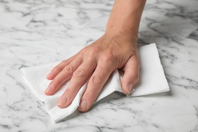 Woman wiping marble table with paper towel, closeup