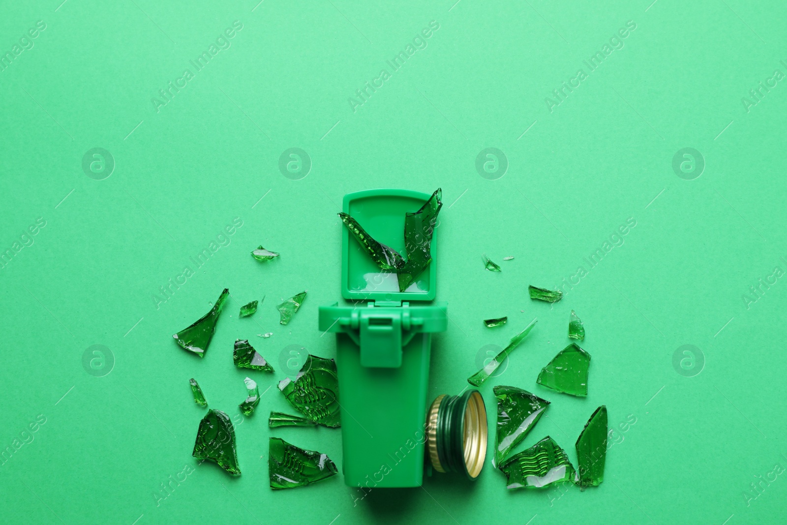 Photo of Mini recycling bin, cap and glass shatters on green background, flat lay. Space for text