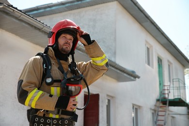 Photo of Firefighter in uniform with helmet near station outdoors, space for text