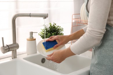 Photo of Woman washing plate at sink in kitchen, closeup