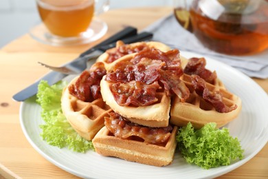 Photo of Tasty Belgian waffles served with bacon, lettuce and tea on wooden table, closeup