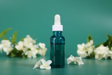 Photo of Essential oil in bottle and beautiful jasmine flowers on green background