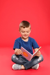 Cute little boy reading book on color background, space for text