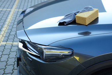 Photo of Sponge and rag on car hood outdoors. Cleaning products
