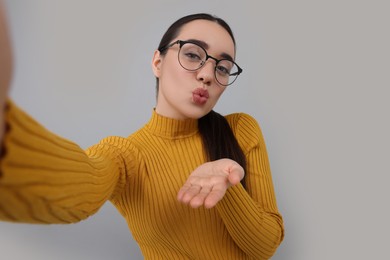 Photo of Young woman taking selfie and blowing kiss on grey background