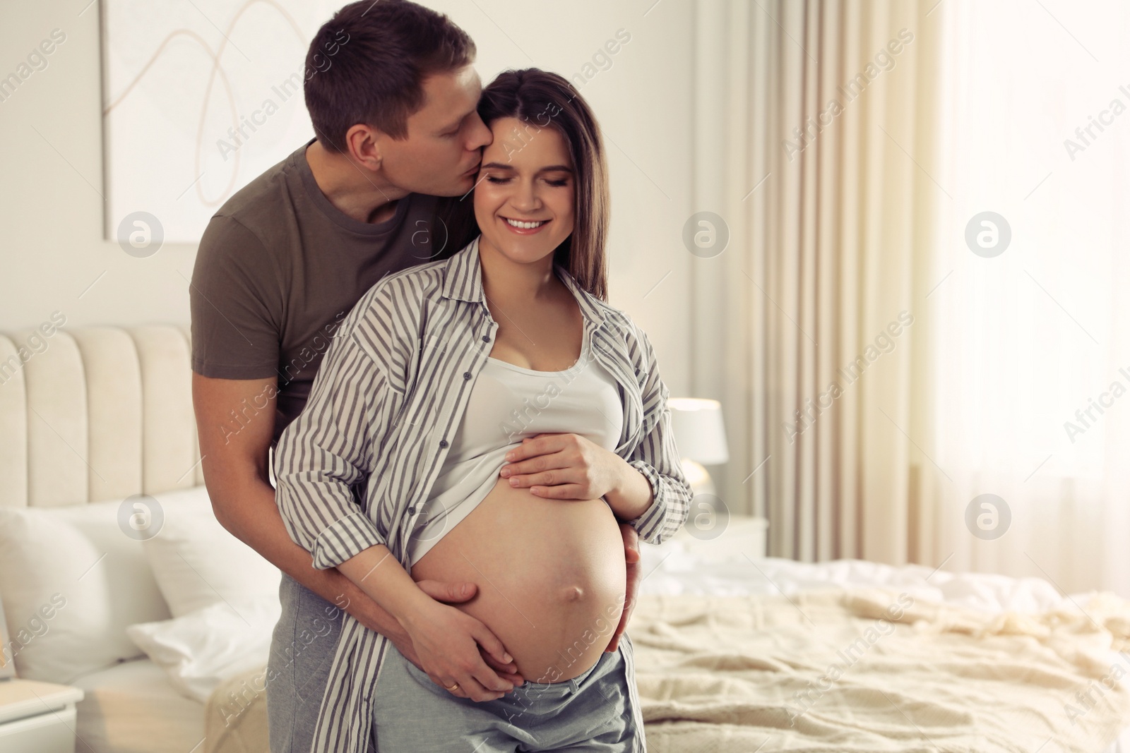 Photo of Young pregnant woman with her husband in bedroom