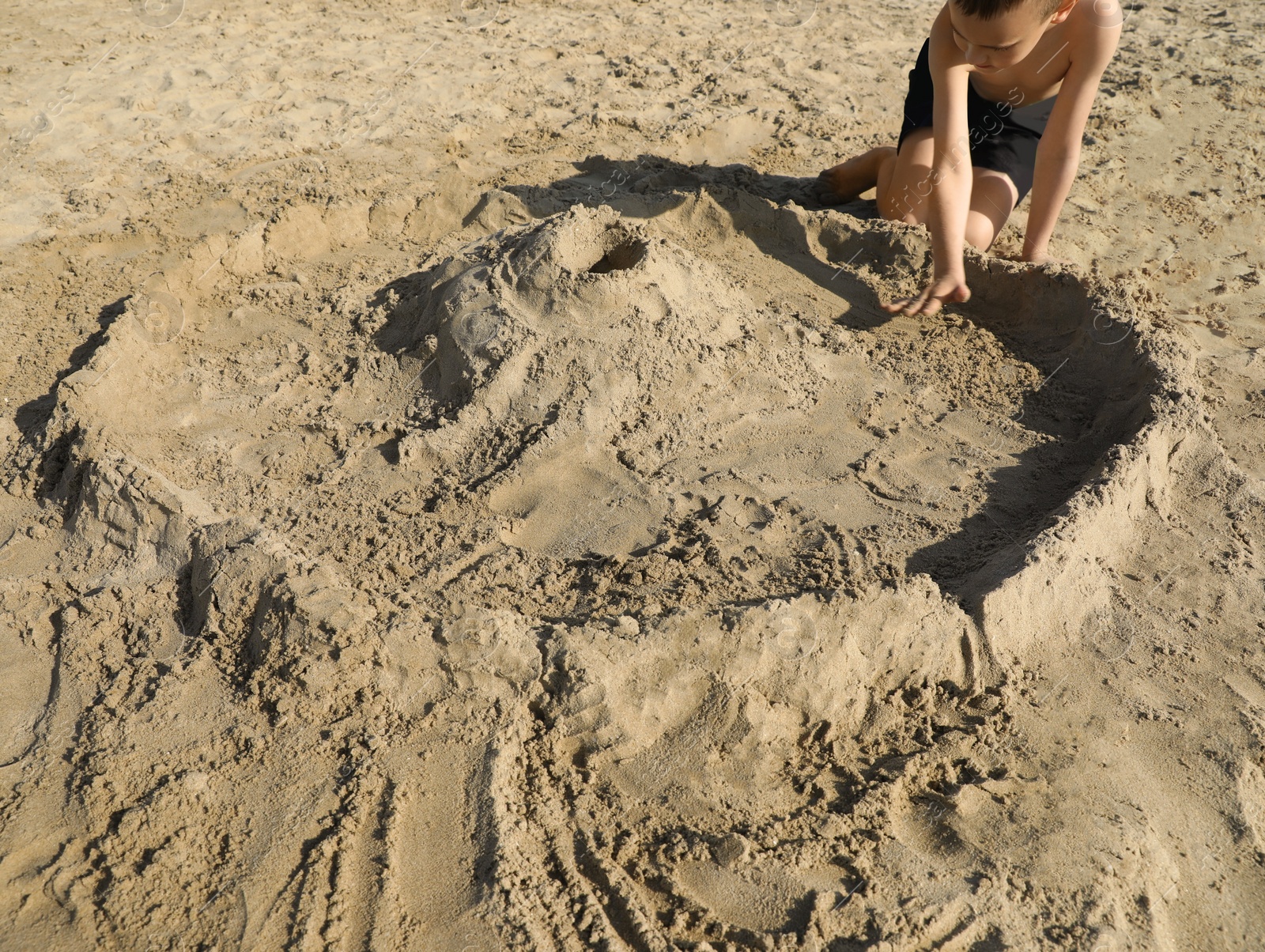 Photo of Little boy playing with sand on sunny day