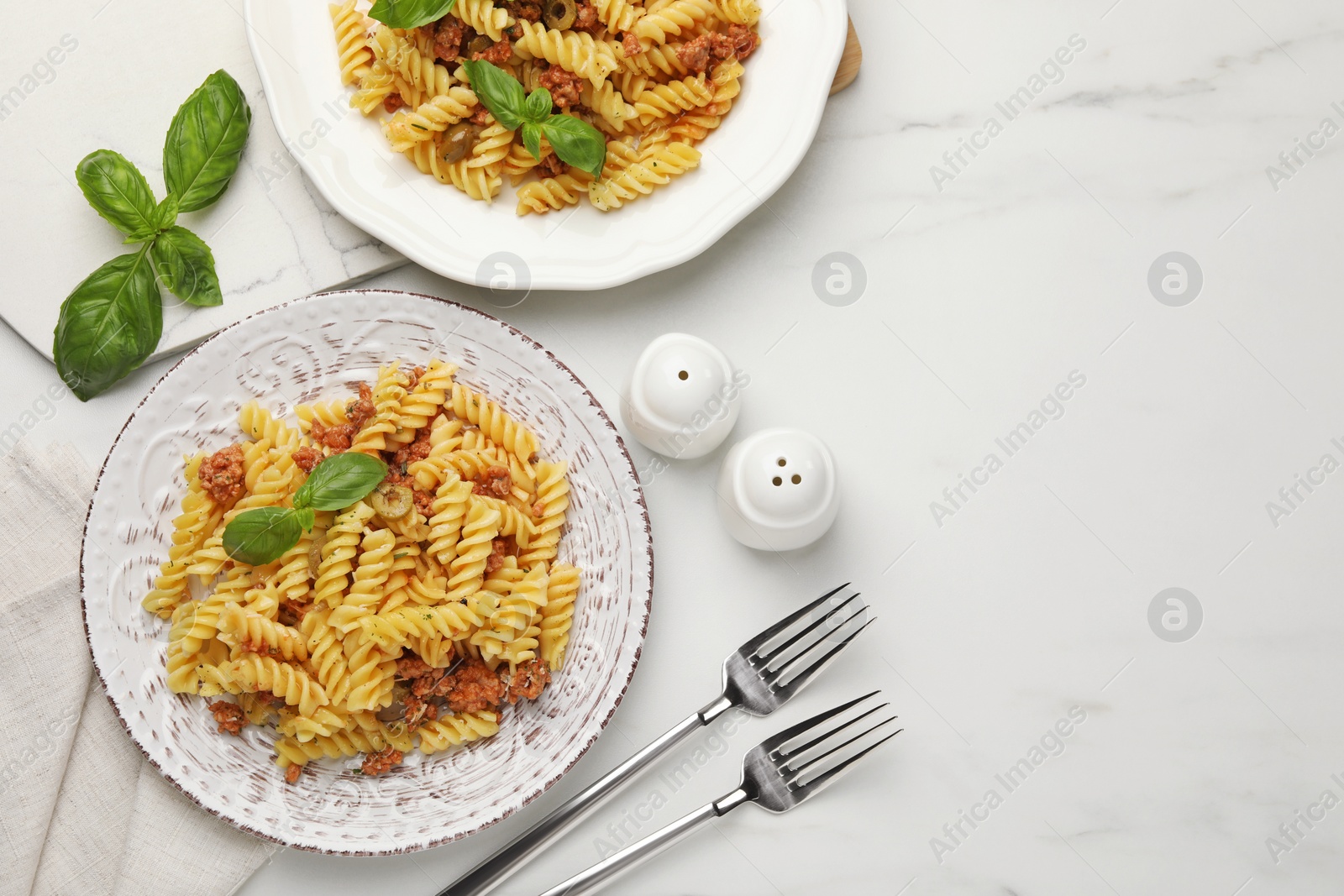 Photo of Delicious pasta with minced meat and basil served on white marble table, flat lay. Space for text