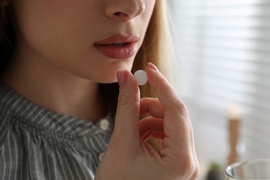 Photo of Young woman taking abortion pill on blurred background, closeup