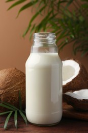 Photo of Glass bottle of delicious vegan milk, coconuts and palm leaves on wooden table