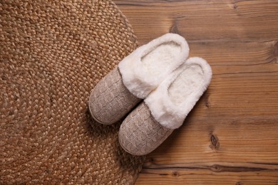 Pair of warm stylish slippers and wicker mat on wooden floor, flat lay