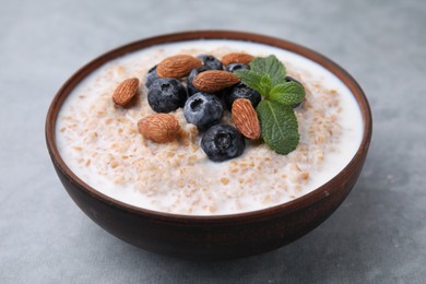 Photo of Tasty wheat porridge with milk, blueberries and almonds in bowl on gray table, closeup