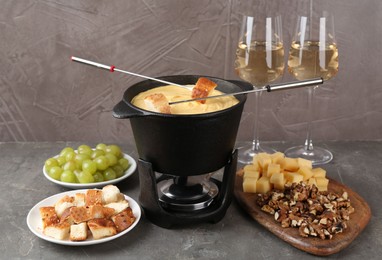 Photo of Fondue pot with tasty melted cheese, forks, wine and different snacks on grey table