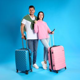 Photo of Happy couple with suitcases and tickets in passports for summer trip on blue background. Vacation travel