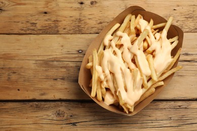 Photo of Delicious French fries with cheese sauce on wooden table, top view. Space for text