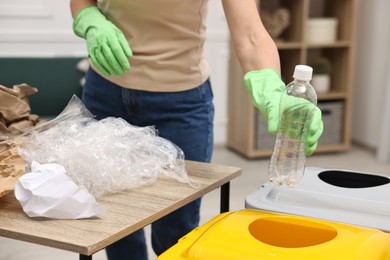 Photo of Garbage sorting. Woman throwing plastic bottle into trash bin in room, closeup