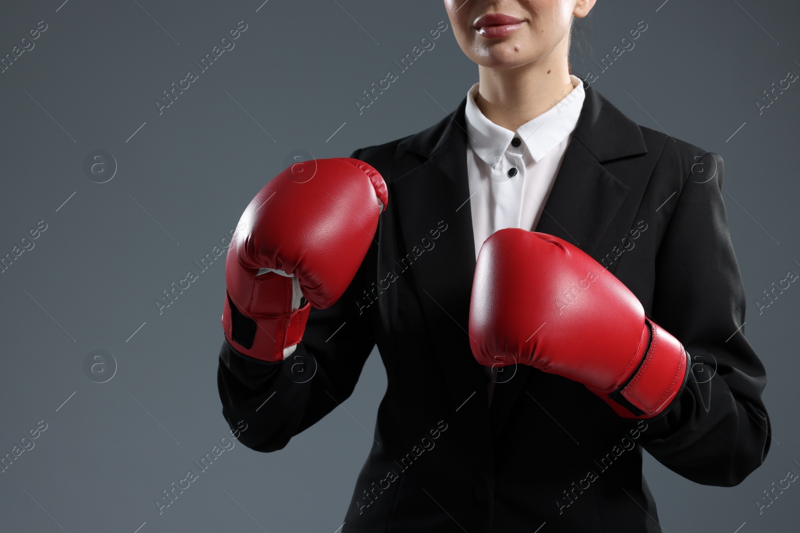 Photo of Businesswoman in suit wearing boxing gloves on grey background, closeup. Space for text