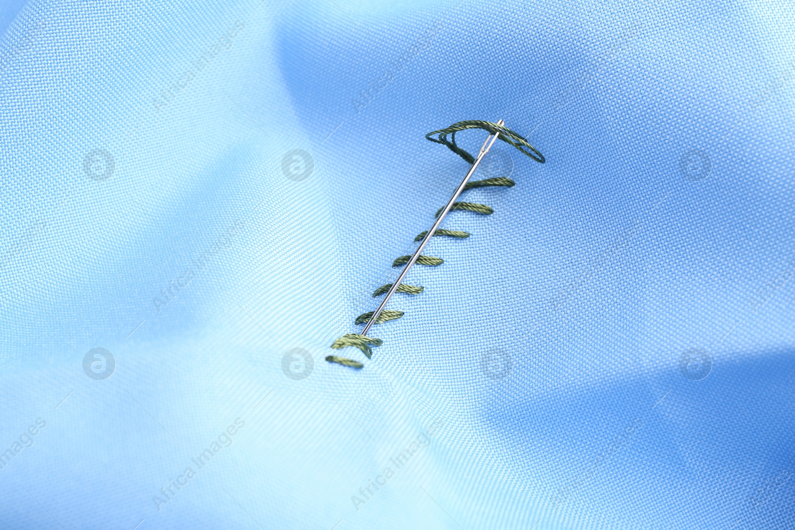 Photo of Sewing needle with thread and stitches on light blue cloth, closeup