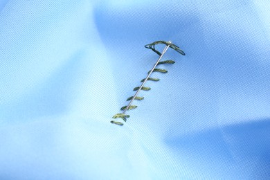 Photo of Sewing needle with thread and stitches on light blue cloth, closeup