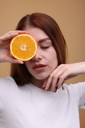 Beautiful woman covering eye with half of orange on beige background