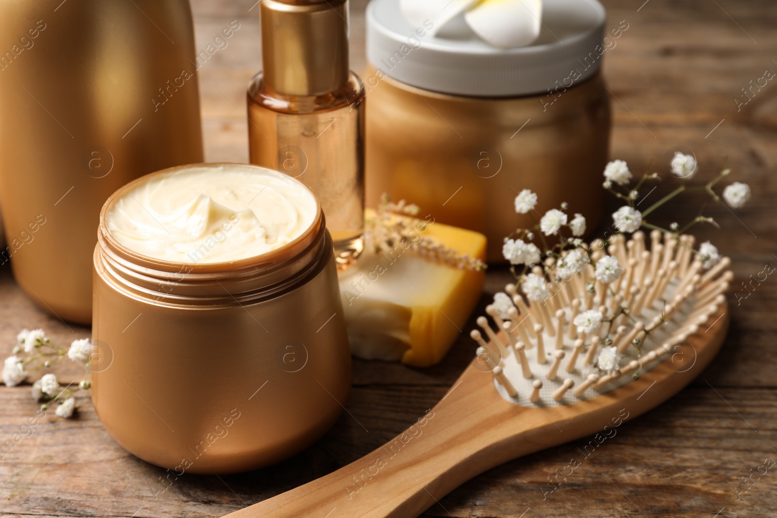 Photo of Set of hair cosmetic products, brush and flowers on wooden table, closeup