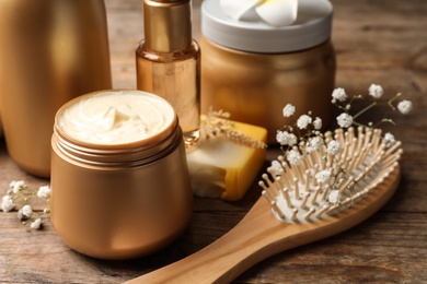 Photo of Set of hair cosmetic products, brush and flowers on wooden table, closeup