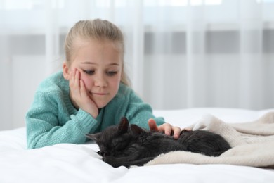 Photo of Little girl with cute fluffy kittens on bed indoors