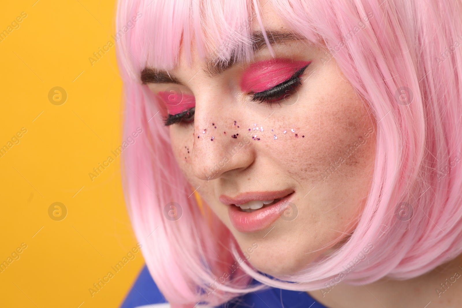 Photo of Beautiful woman with bright makeup and glitter freckles on yellow background, closeup