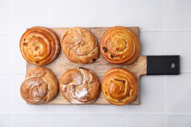 Delicious rolls with raisins and powdered sugar on white tiled table, top view. Sweet buns