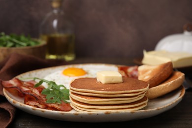 Tasty pancakes served with fried eggs and bacon on wooden table, closeup