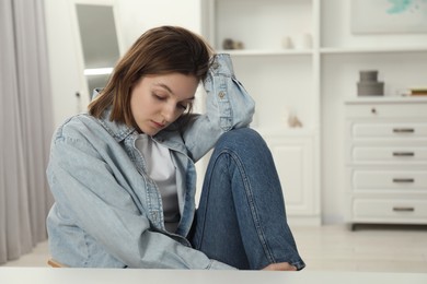 Photo of Sad young woman sitting at white table in room