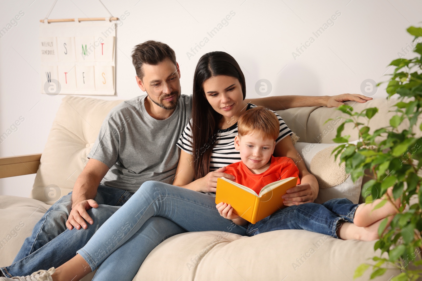 Photo of Happy family reading book together on sofa in living room at home