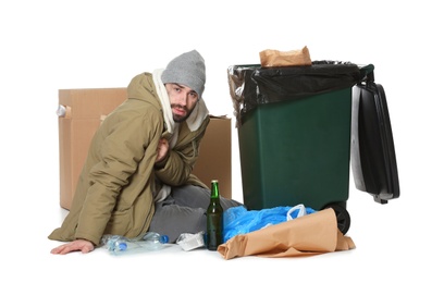 Photo of Poor homeless man sitting near trash bin isolated on white