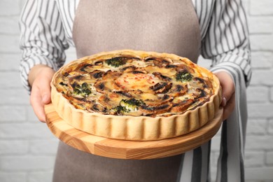 Photo of Woman holding delicious homemade quiche with mushrooms near white brick wall, closeup