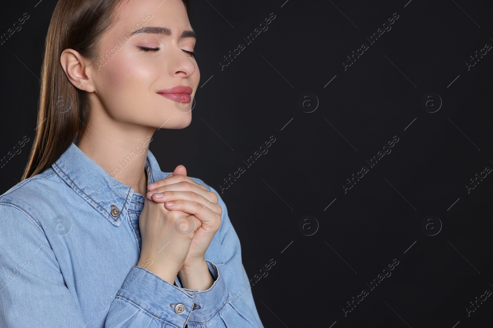 Photo of Woman with clasped hands praying on black background, space for text