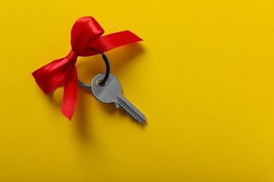 Photo of Key with red bow on yellow background, top view. Space for text. Housewarming party
