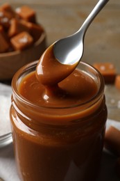 Taking yummy salted caramel with spoon from glass jar at table, closeup