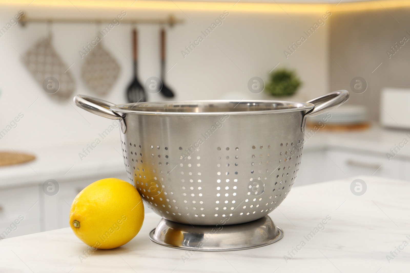 Photo of Empty colander and fresh lemon on white marble table in kitchen