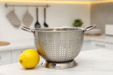 Photo of Empty colander and fresh lemon on white marble table in kitchen