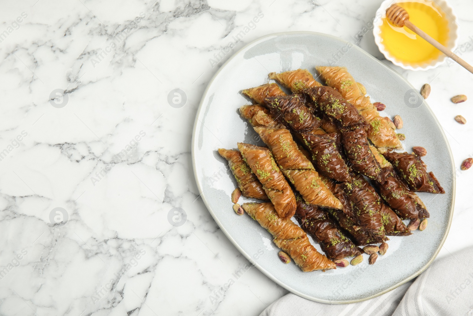 Photo of Delicious baklava with pistachio nuts and honey on white marble table, flat lay. Space for text