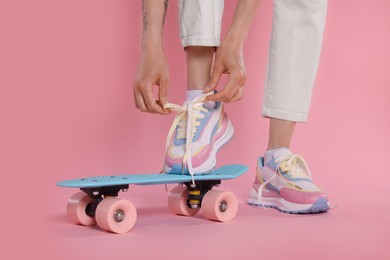 Photo of Woman tying lace of sneaker on skateboard against pink background, closeup