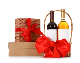 Festive basket with bottles of wine and gift boxes on white background