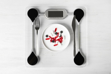 Photo of Scales with weight loss pills and cutlery on wooden background, top view