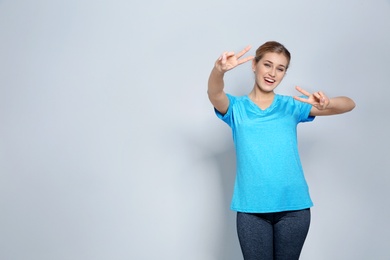 Photo of Happy young woman showing victory gesture on color background. Space for text