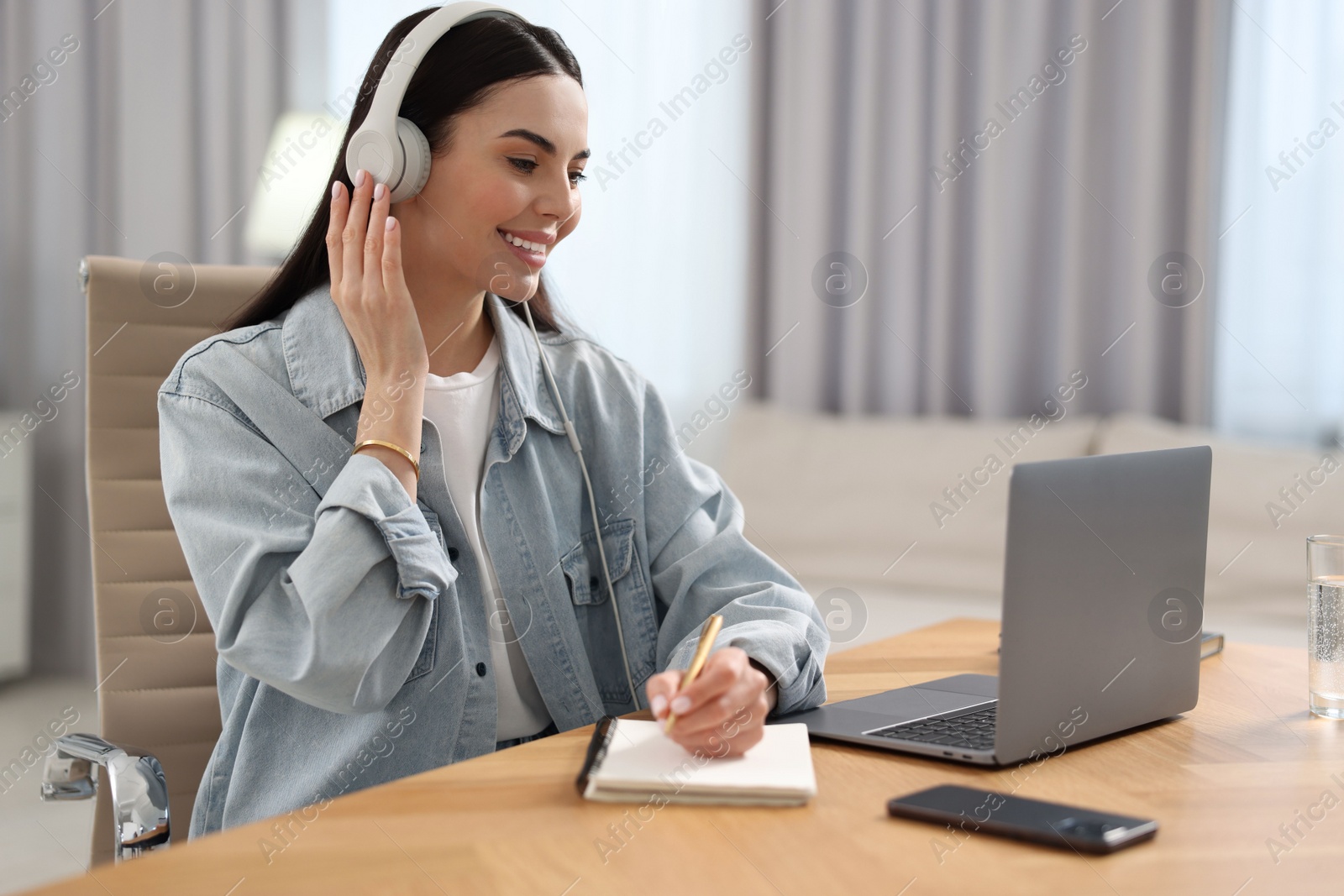 Photo of Young woman in headphones watching webinar at table in room