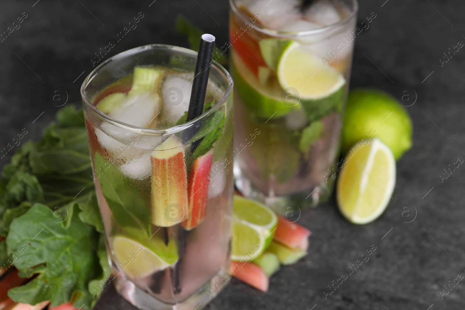 Photo of Tasty rhubarb cocktail with lime on black table, closeup. Space for text